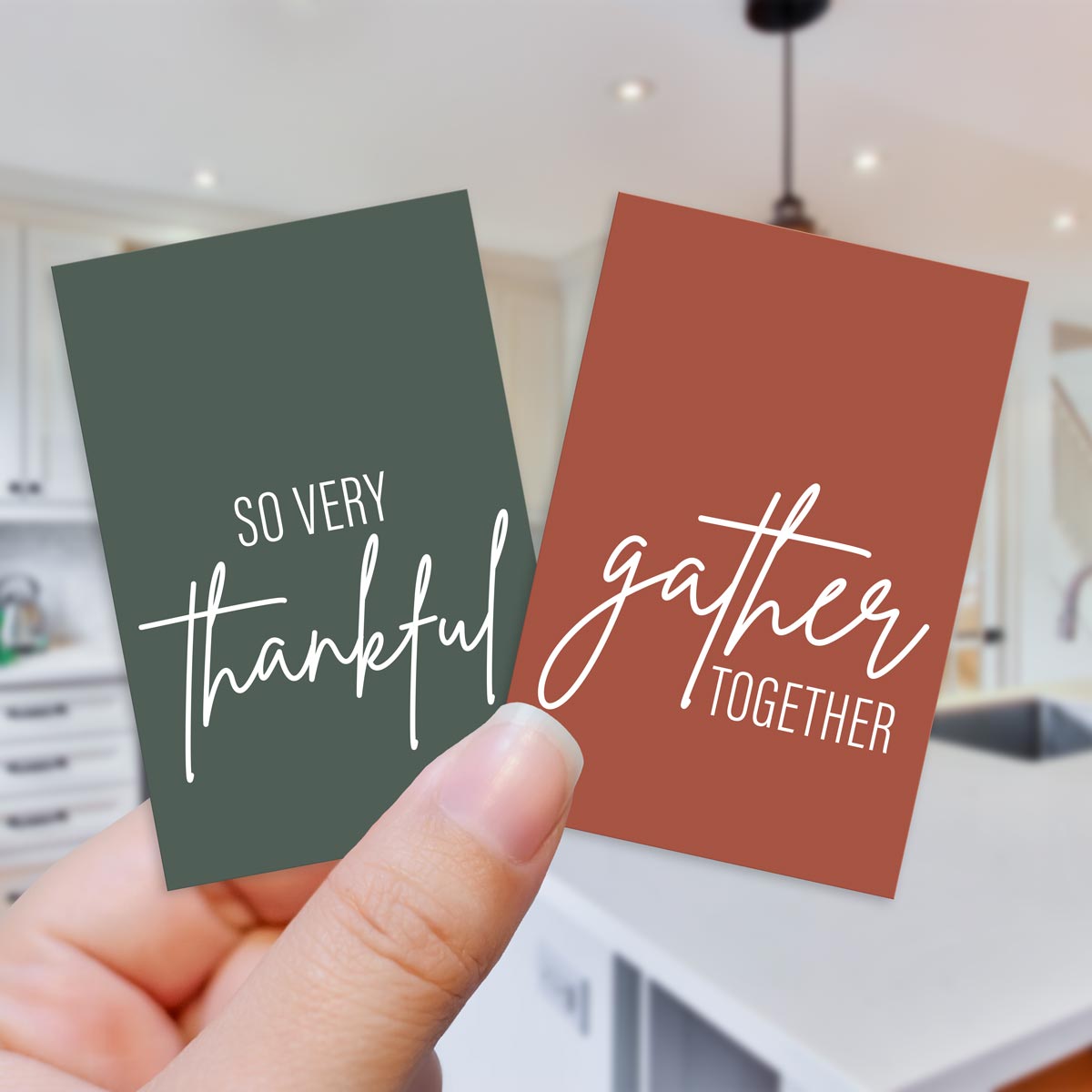 Two gift cards with 'So very thankful' and 'gather together' text held in a hand, with a blurred kitchen background.
