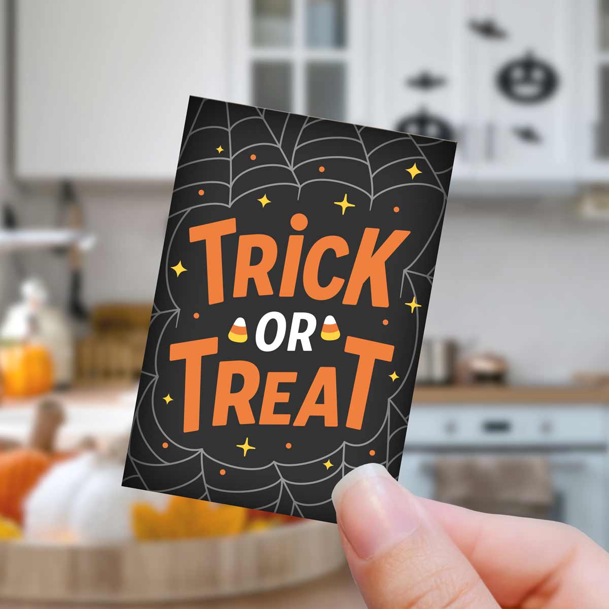 Halloween-themed 'Trick or Treat' card held in a hand with a kitchen background.